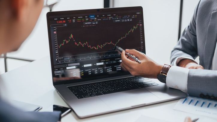 A closeup of a person pointing to a stock chart on a laptop. 
