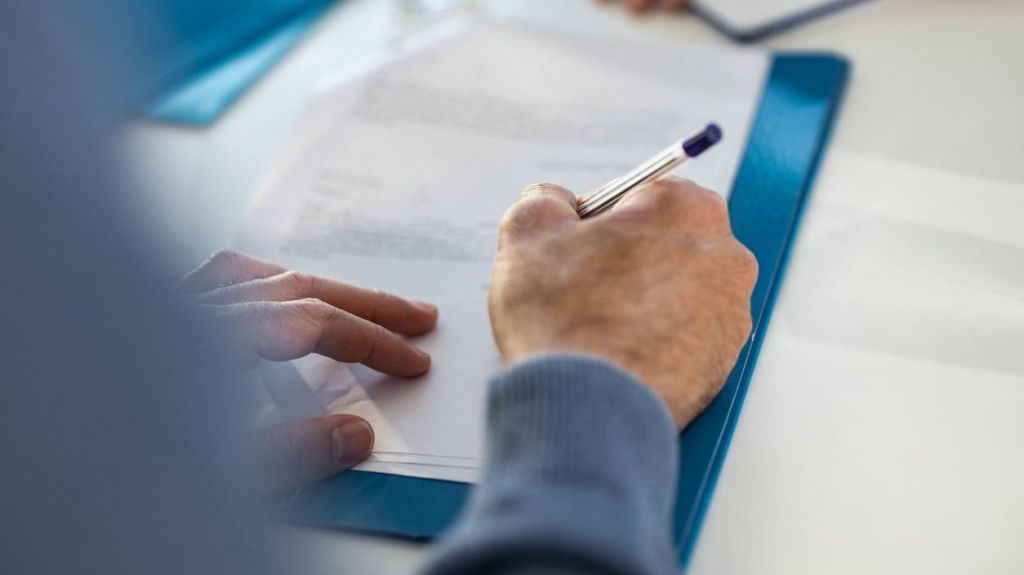 A close up of a man signing a lease document in an office.