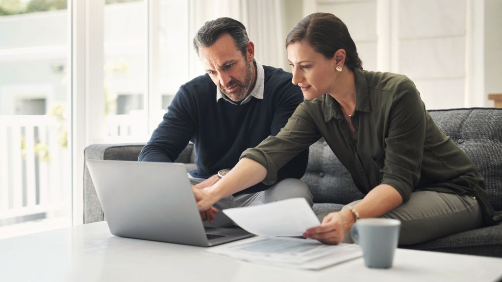 A woman and man look over data on a laptop while sitting together on a couch.