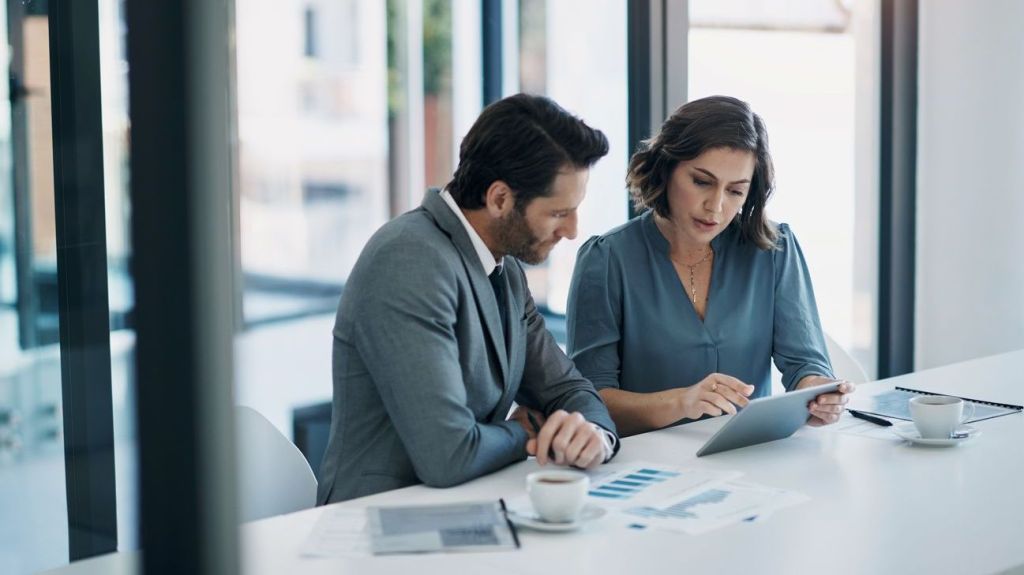 A man and woman look over data on a tablet. 