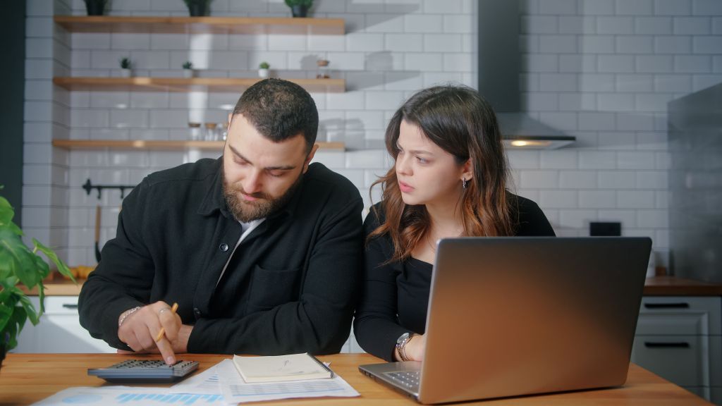 A young couple sits in their kitchen and reviews their finances together.