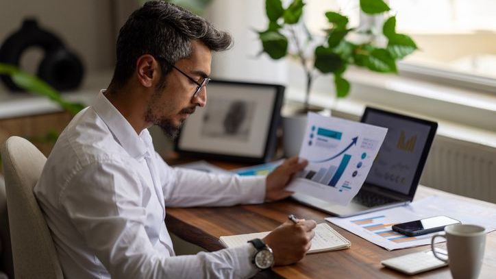 A man takes notes while looking over financial charts and data. 