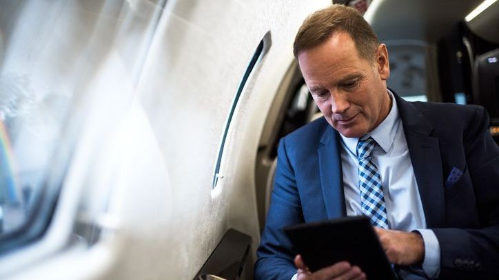 A man in a suit looks at his tablet while sitting on a private jet. 
