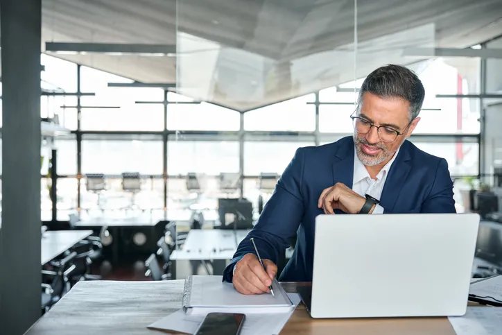 Man working on laptop computer and writing notes.