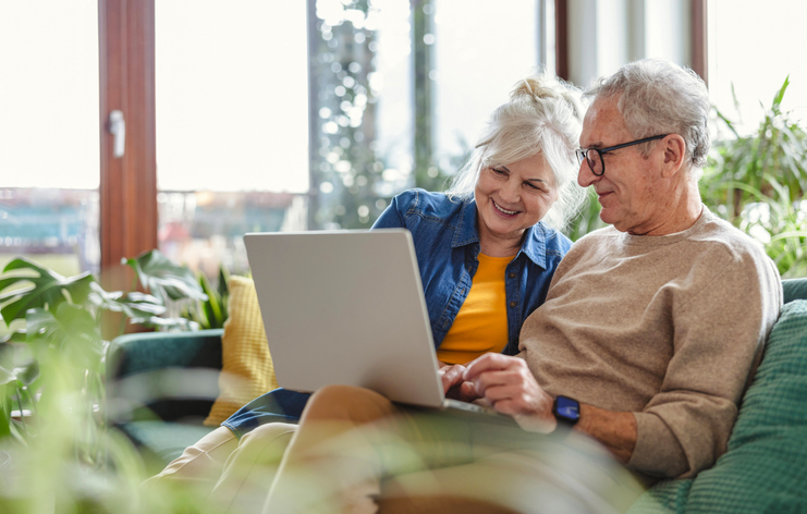 A retired couple using a laptop in their living room to manage their retirement investments.