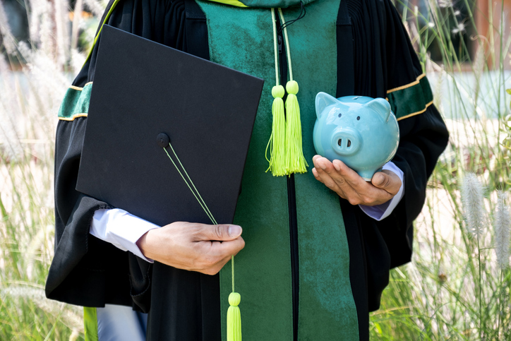 Graduating student holding a cap and piggy bank.