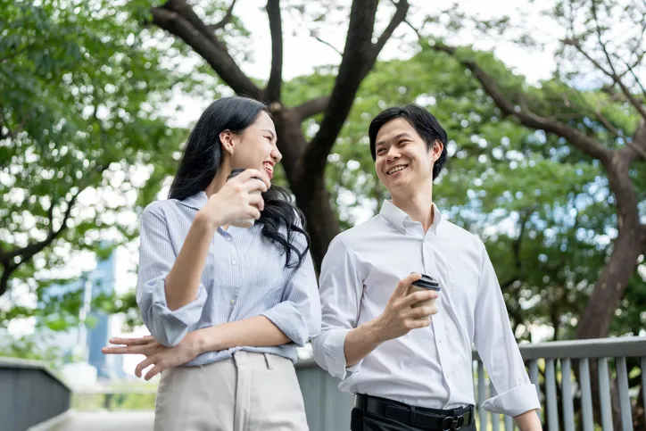 Businessman and woman hold a cup of coffee outdoors in the park.