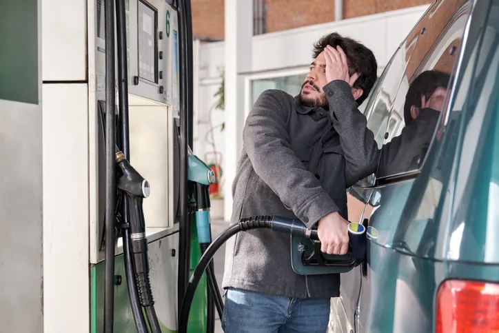 Young man refueling his vehicle, looking worried at the high gas prices at a gas station.