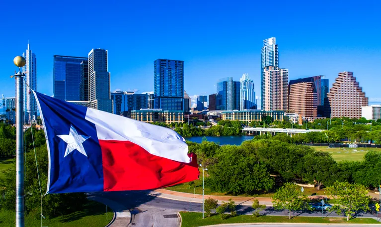 Texas flag flying in front of the Austin, Texas skyline.