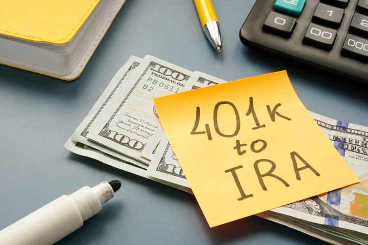 "401k to IRA" written on a sticky note attached to a stack of cash.