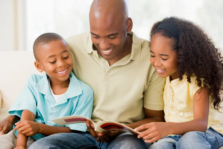 A father reads a book with his son and daughter.